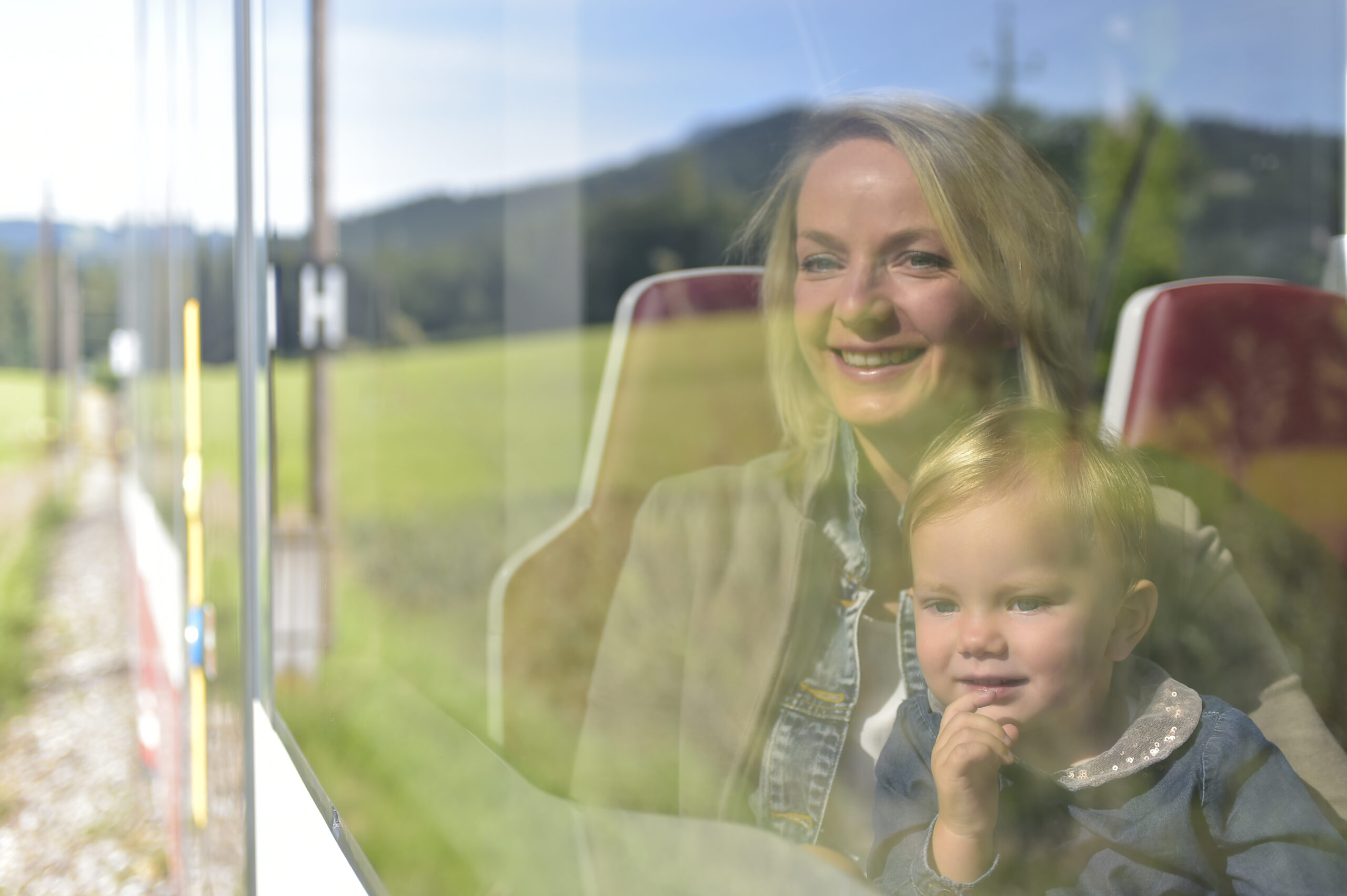 Eine Frau mit Kind sitzt in der Traunseetram hinter einer Glasscheibe