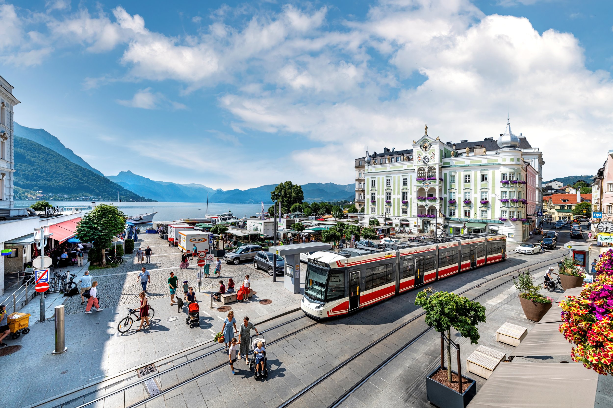 Die Traunseetram vor dem Rathausplatz Gmunden, im Hintergrund sieht man den Traunsee und das Bergpanorama